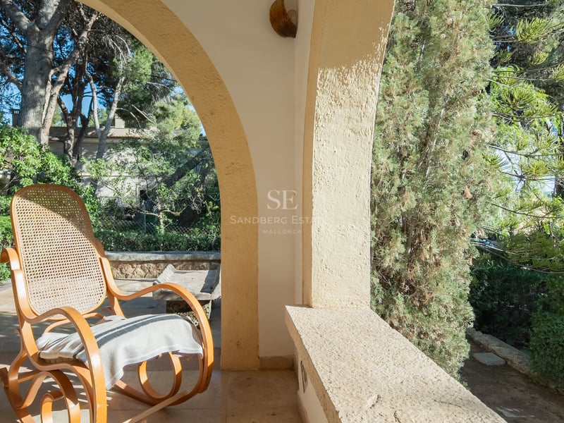 Un fauteuil à bascule classique sur une terrasse voûtée en pierre surplombant un jardin verdoyant.