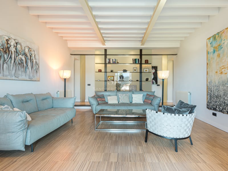 Grand salon avec canapés bleu clair, plafond à poutres blanches, parquet et grandes peintures abstraites.