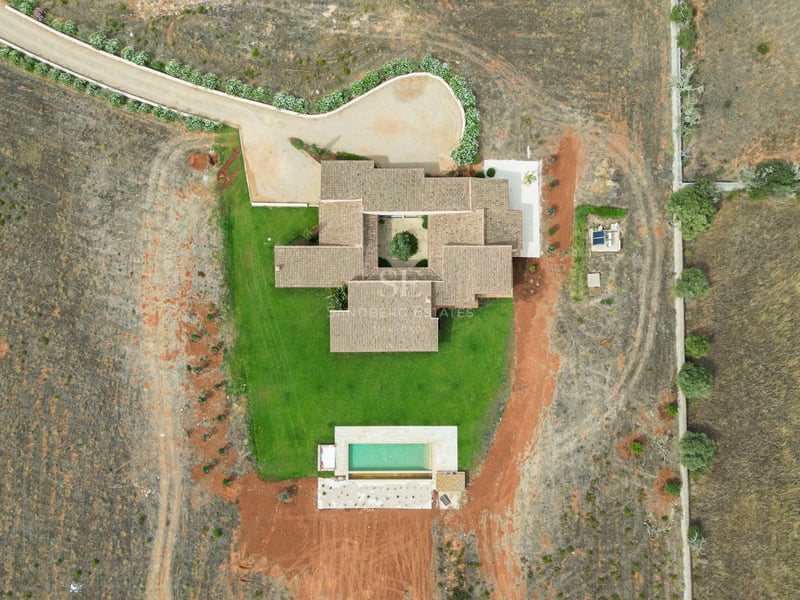Vue de dessus par drone d'une villa avec toit en tuiles, patio intérieur central, pelouse et piscine rectangulaire.