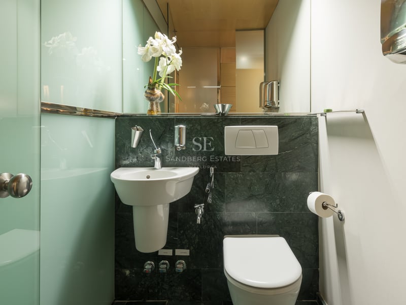Bathroom featuring dark green marble walls, white porcelain sink, and frosted glass partitions.