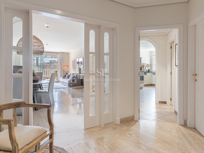 Vue depuis un hall en marbre vers un salon et une cuisine, avec des portes coulissantes blanches et du bois naturel.