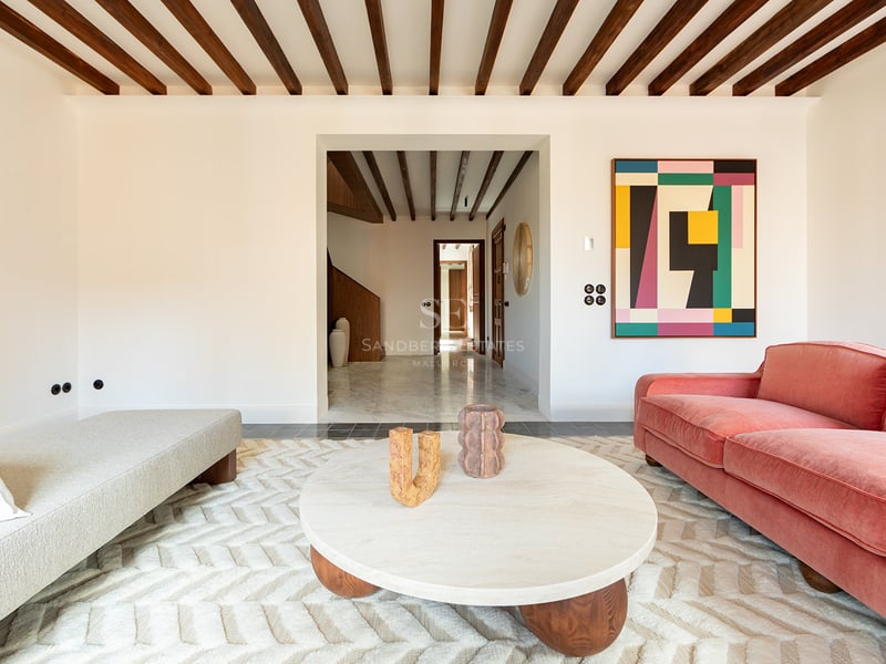 Salón moderno con vigas de madera oscura, sofá color terracota, mesa de mármol redonda y alfombra con textura.