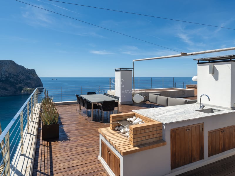 Terrasse de luxe sur le toit avec cuisine extérieure, coin repas et vue panoramique sur une baie méditerranéenne.