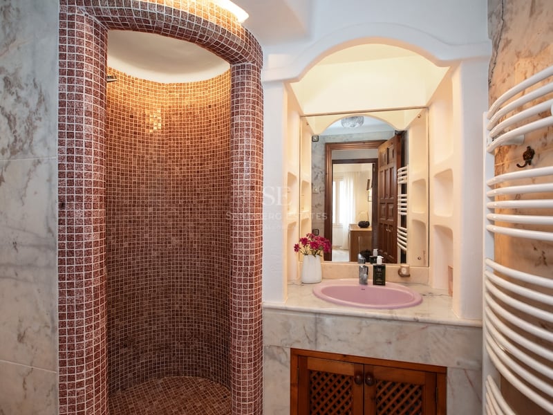 Douche à l'italienne courbe en mosaïque rougeâtre à côté d'un meuble vasque en marbre avec un évier rose.