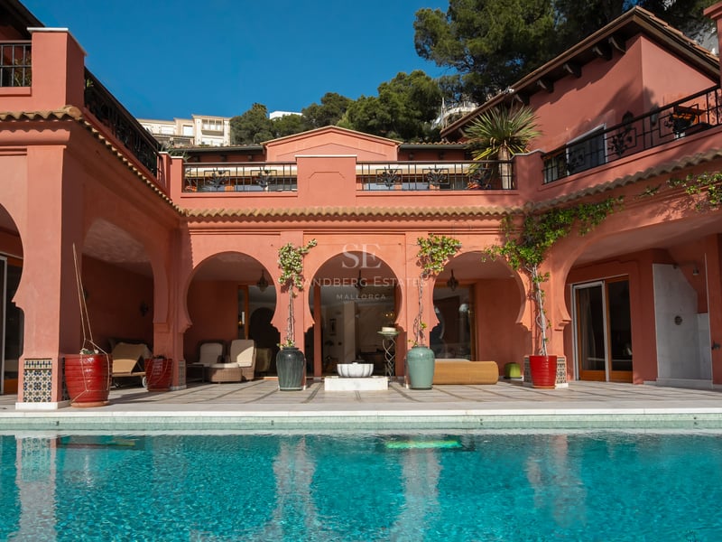Façade de villa de luxe aux murs terre cuite avec arches mauresques donnant sur une piscine bleu turquoise.