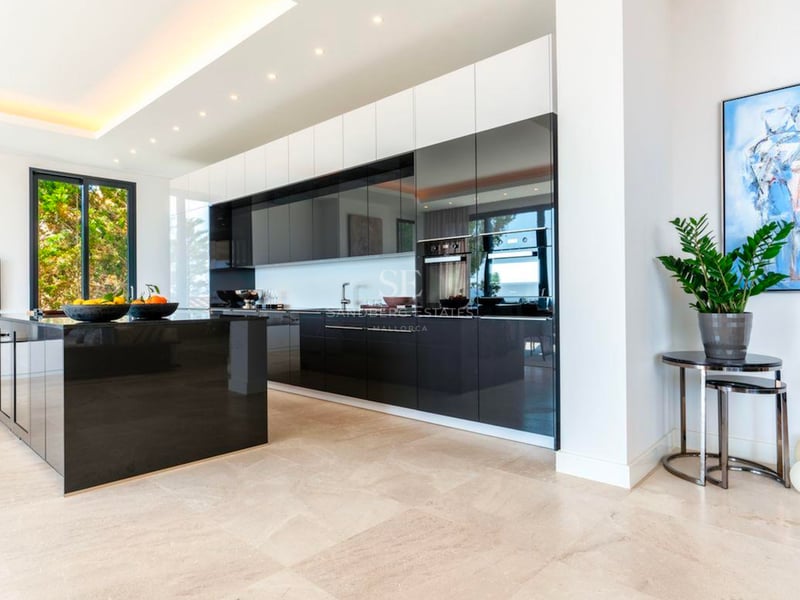 Grande cuisine moderne avec un îlot noir brillant, des placards sombres et un sol en pierre claire.