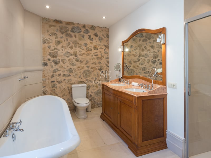 Salle de bain avec mur en pierre, double vasque en bois, baignoire îlot et douche vitrée.