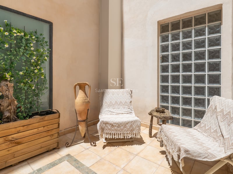 Patio ensoleillé avec deux chaises longues, une amphore en terre cuite et un mur en briques de verre.