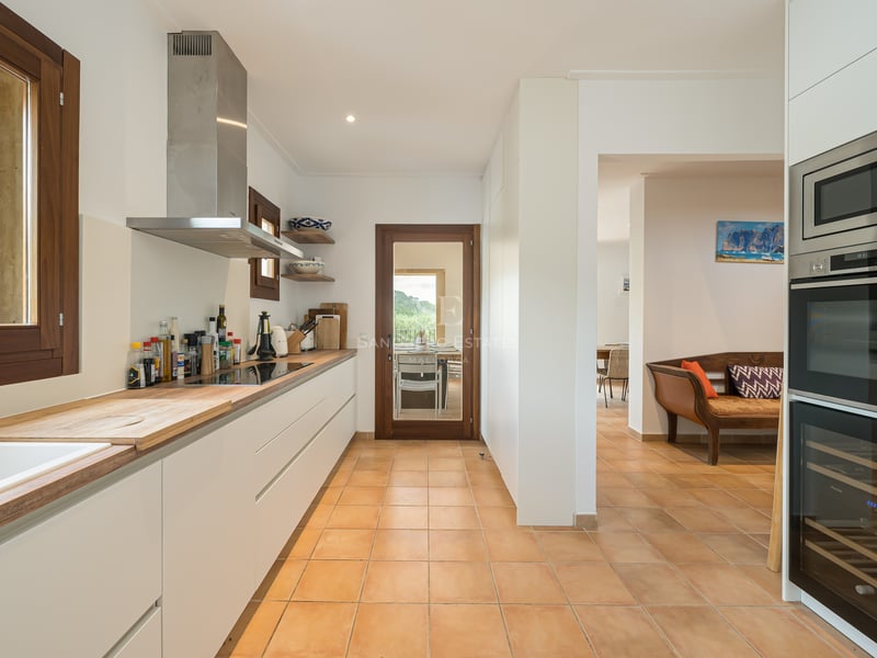 Cuisine blanche moderne avec plans de travail en bois, sol en terre cuite et hotte aspirante en acier inoxydable.
