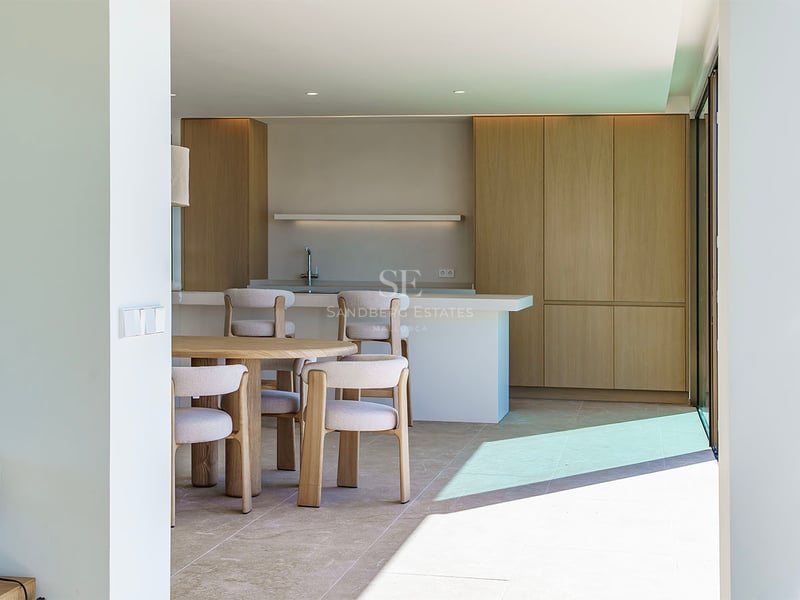 Cuisine moderne lumineuse avec placards en chêne clair, îlot en pierre blanche et table à manger circulaire en bois.