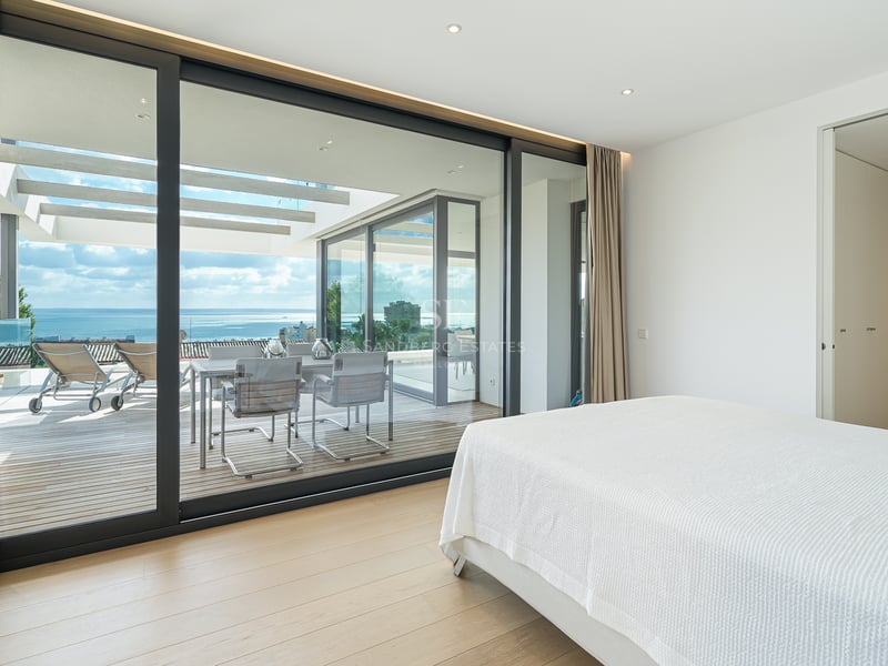 Chambre moderne avec lit blanc et grandes baies vitrées ouvrant sur une terrasse avec vue mer.