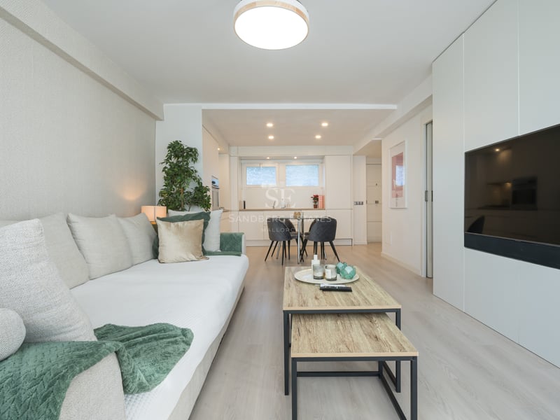 Salon lumineux avec canapé blanc, parquet clair et grand téléviseur intégré dans un meuble mural blanc.
