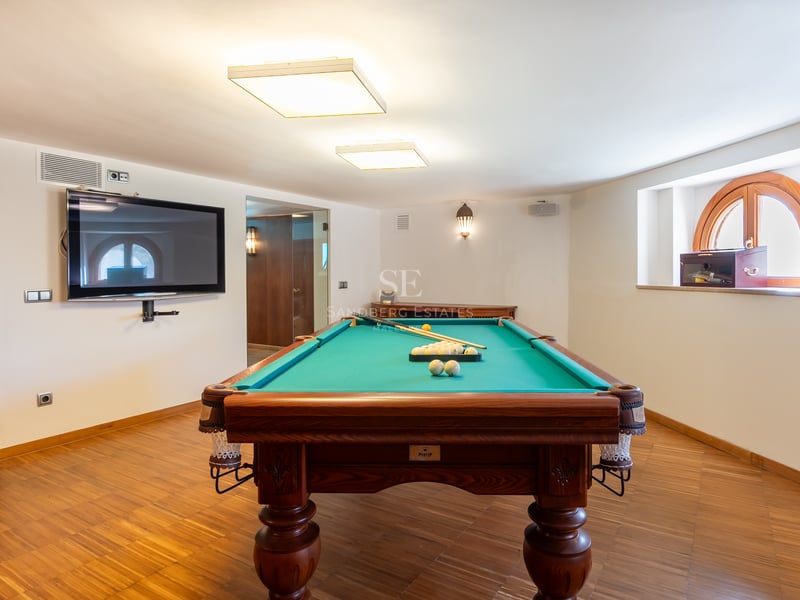 Table de billard en bois et tapis vert dans une salle de jeux moderne avec parquet et télévision murale.