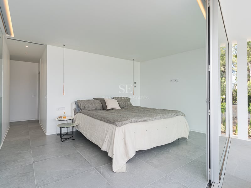 Chambre minimaliste avec sol en pierre grise, murs blancs et grande baie vitrée coulissante donnant sur le jardin.