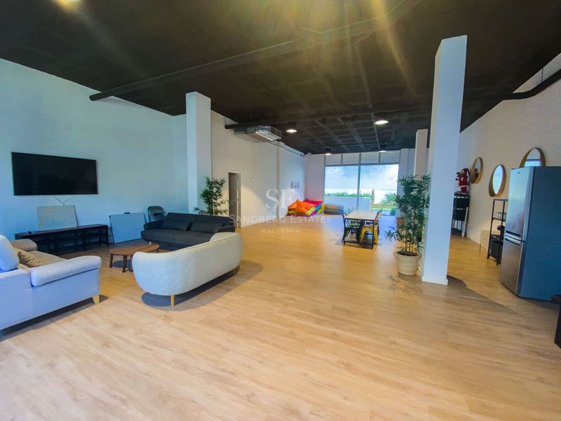 Grande pièce à aire ouverte avec parquet clair, canapés, table à manger, poufs colorés et accès extérieur.