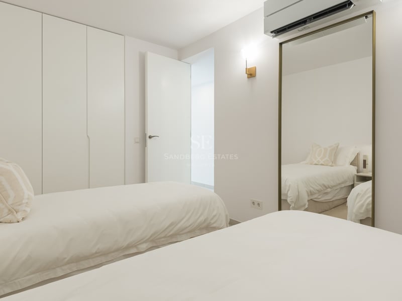 Chambre minimaliste lumineuse avec deux lits simples, de grandes armoires blanches et un miroir avec cadre doré.