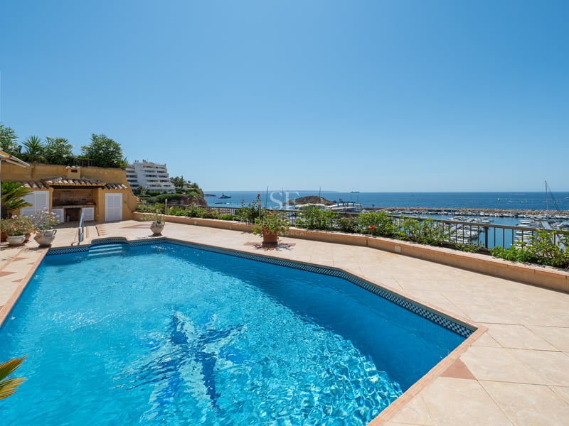 Piscine ensoleillée sur une terrasse en terre cuite surplombant une marina méditerranéenne et la mer bleue.