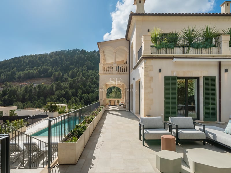 Terrasse de luxe avec mobilier moderne surplombant une piscine et des montagnes boisées sous un ciel bleu clair.