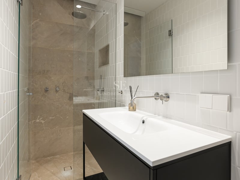 Salle de bain moderne avec carrelage blanc, meuble noir et douche à l'italienne avec parois en verre.