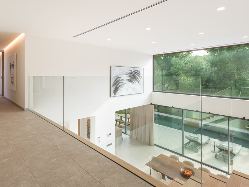 Vue depuis une mezzanine en verre sur un salon à double hauteur avec de grandes baies vitrées donnant sur la piscine.