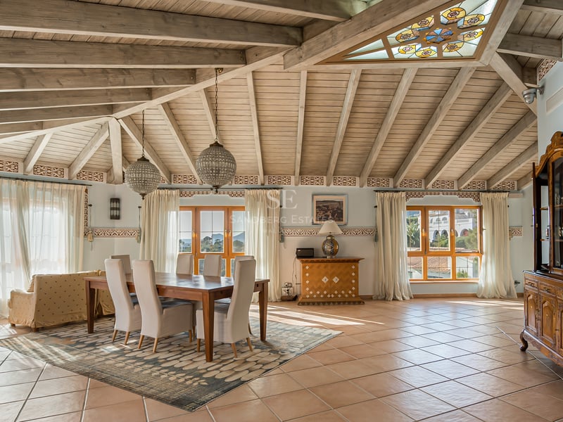 Salle à manger avec plafond voûté en bois, carreaux de terre cuite et grandes fenêtres lumineuses.