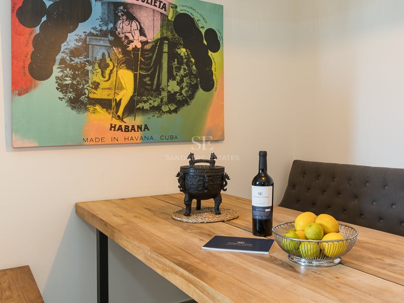 Table à manger en bois massif avec banc rembourré gris, bouteille de vin, bol de citrons et tableau vintage cubain.