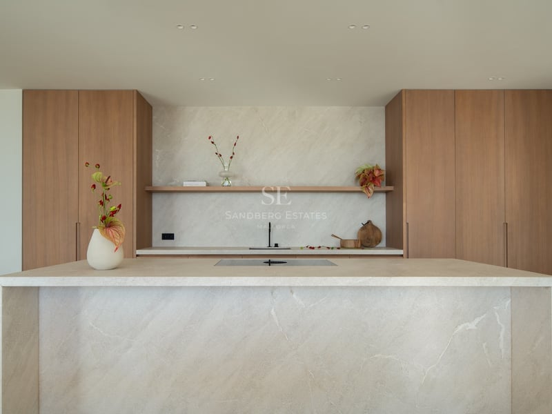 Cuisine moderne avec un grand îlot en pierre beige, des armoires en bois naturel et une étagère flottante.