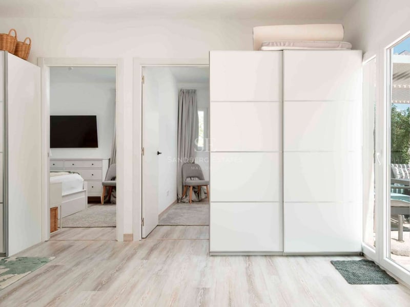 Couloir intérieur lumineux avec de grands placards blancs coulissants et un sol en bois clair menant à une chambre.