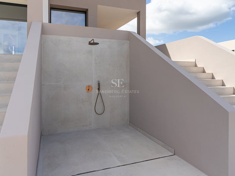 Douche extérieure minimaliste avec murs en microciment gris clair et robinetterie en laiton.