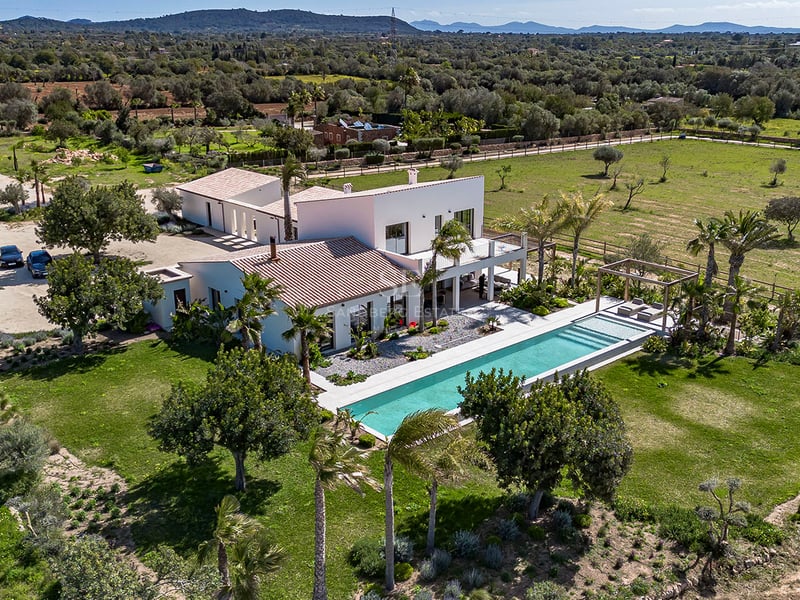 Vue aérienne d'une grande villa blanche avec une longue piscine, entourée de pelouses et de palmiers.
