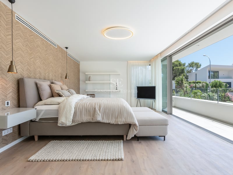 Chambre moderne avec baies vitrées ouvrant sur une terrasse, tons neutres et mur d'accent à motifs chevrons.