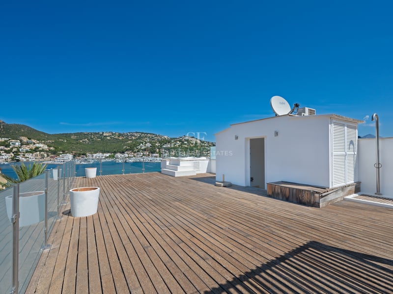 Grande terrasse de toit en bois avec garde-corps en verre offrant une vue sur une marina méditerranéenne.