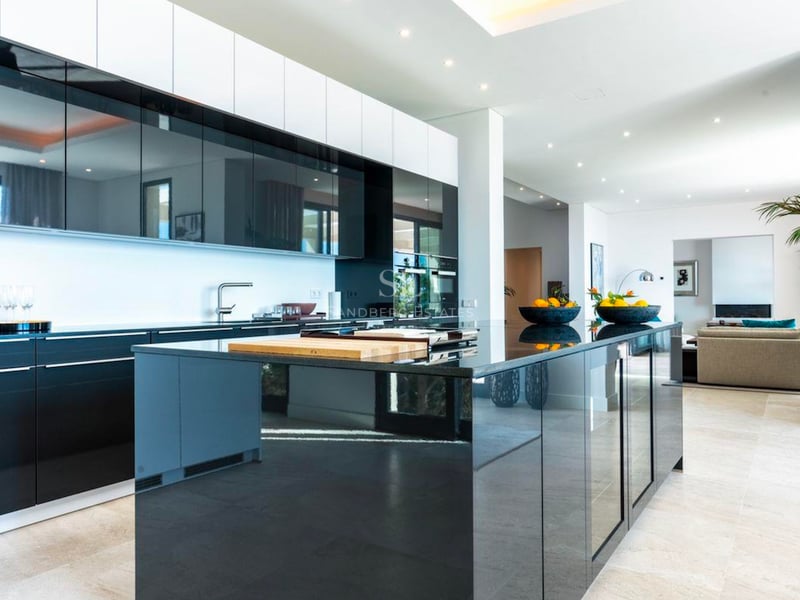 Cuisine de luxe à aire ouverte avec des armoires noir brillant, un grand îlot central et un design contemporain.