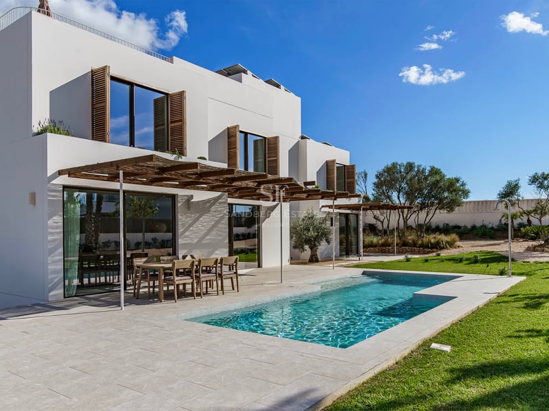 Extérieur d'une villa blanche moderne avec piscine, pergola en bois et pelouse sous un ciel bleu.