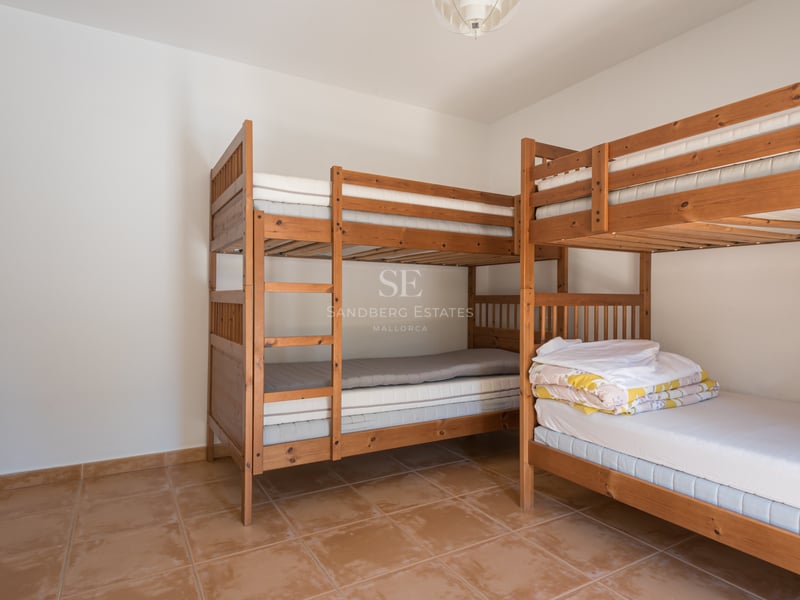 Une chambre lumineuse avec deux lits superposés en bois et un sol en terre cuite.
