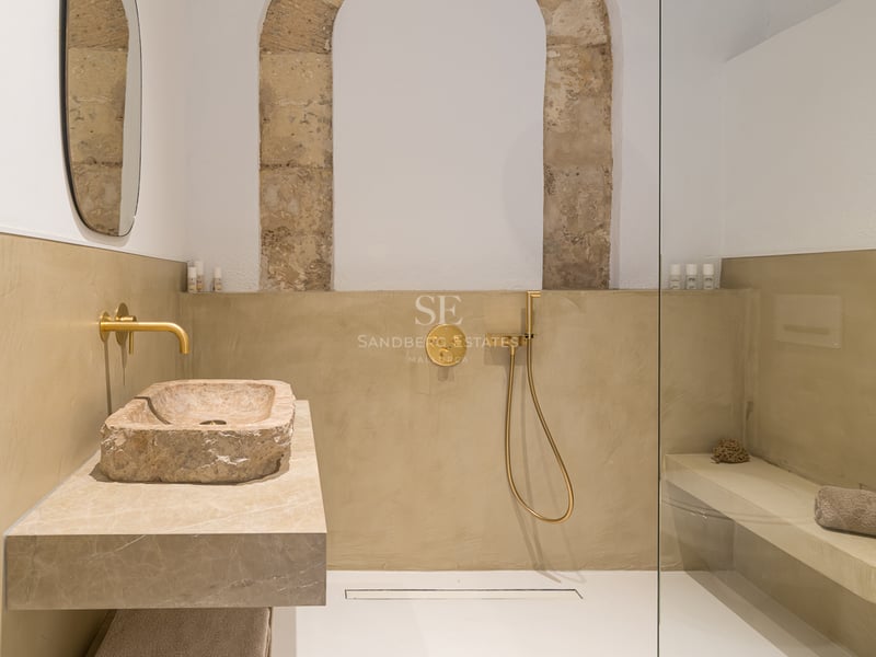 Salle de bain moderne avec vasque en pierre brute, robinetterie dorée et douche à l'italienne avec arche en pierre.