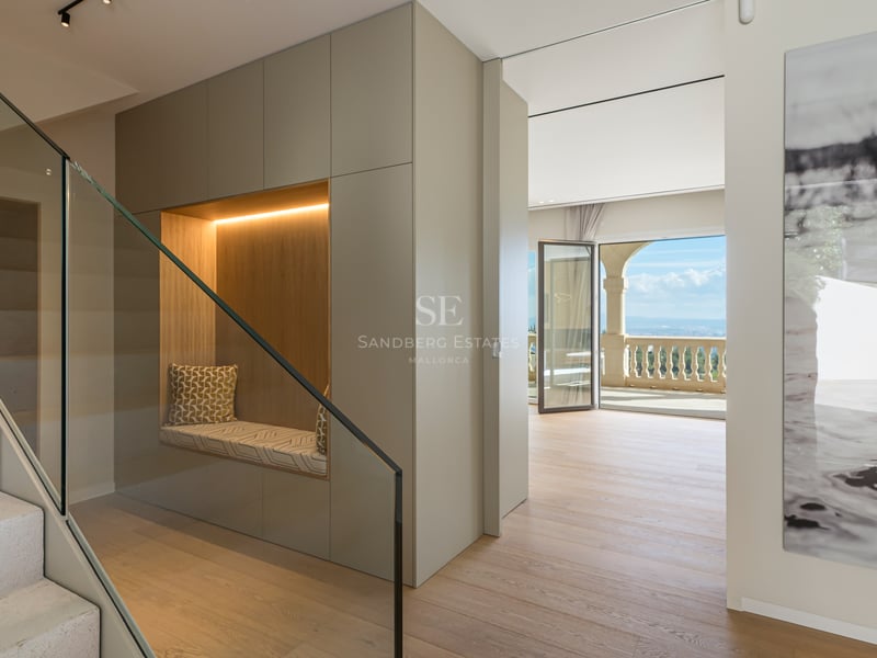 Couloir moderne avec escalier en pierre, garde-corps en verre, alcôve de lecture intégrée et vue mer.