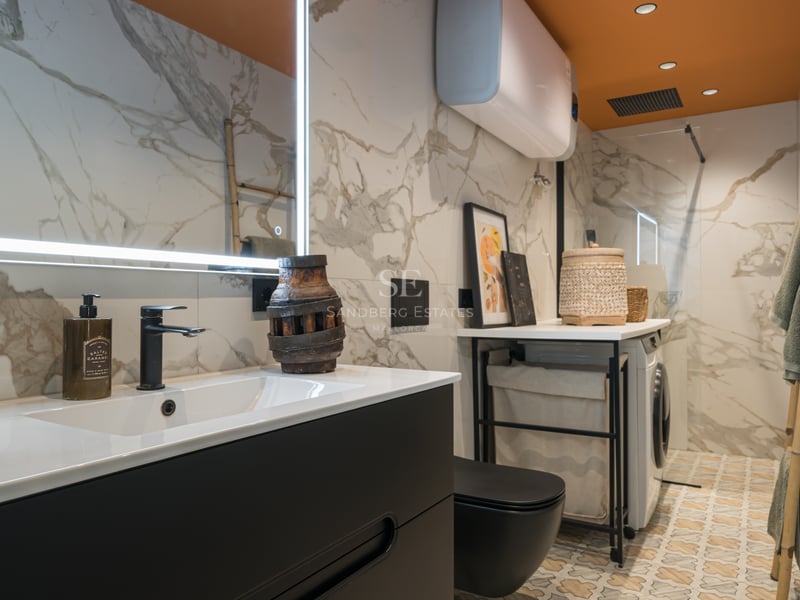 Salle de bain moderne avec murs en marbre, meuble noir mat, sol à motifs et coin buanderie intégré.