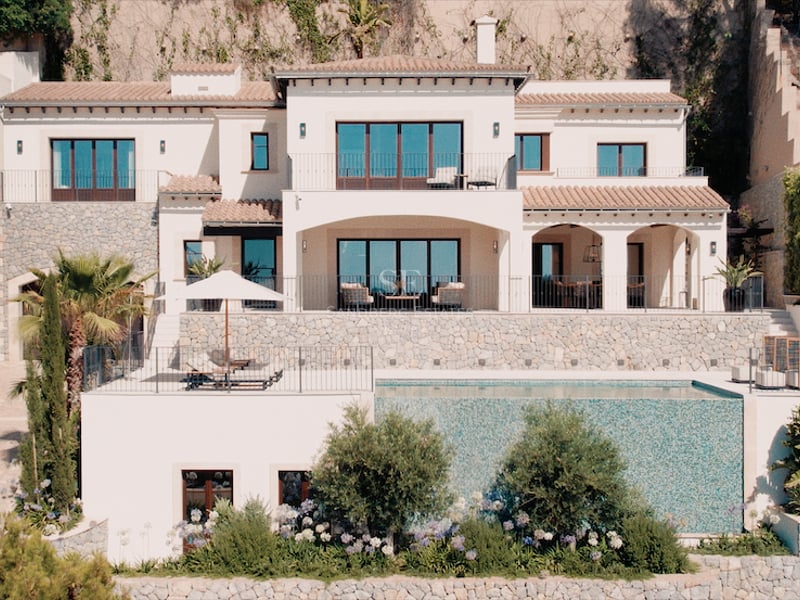 Vue extérieure d'une villa blanche à plusieurs niveaux avec une piscine à débordement et des murs en pierre.