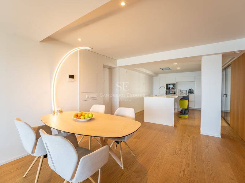 Salle à manger minimaliste avec table en bois clair, chaises grises et lampadaire arqué original.