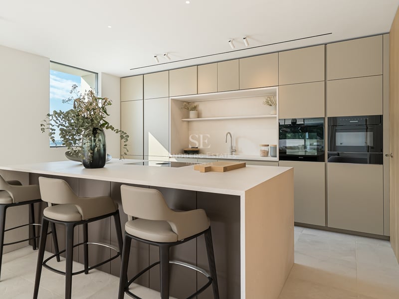 Cuisine moderne minimaliste avec un grand îlot central, des tabourets design et des armoires lisses aux tons terreux.