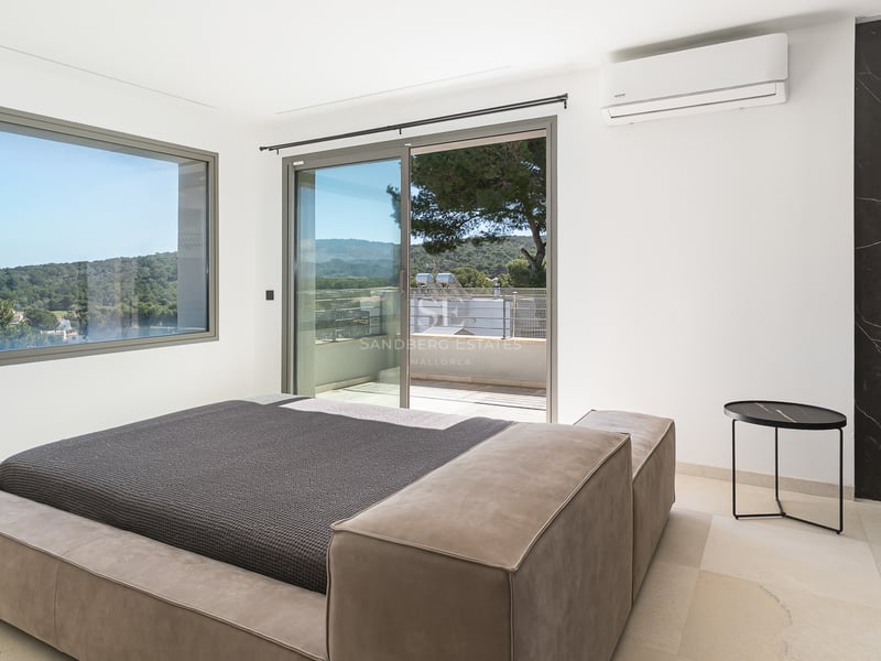 Chambre moderne avec lit bas, grandes baies vitrées coulissantes ouvrant sur une terrasse et vue sur les collines.
