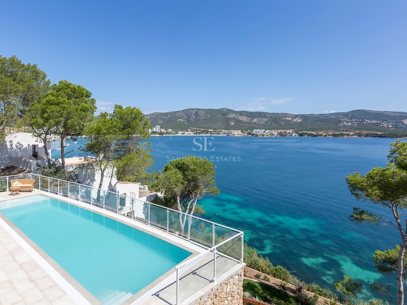 Piscine rectangulaire surélevée avec garde-corps en verre surplombant une baie méditerranéenne aux eaux turquoise.