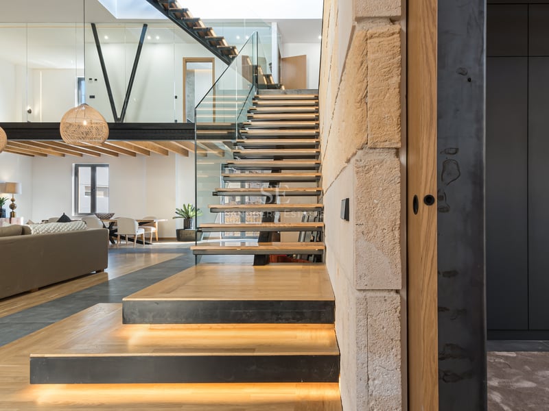 Salon moderne ouvert avec escalier flottant en bois, éclairage LED, garde-corps en verre et mezzanine.