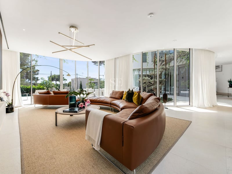 Salon moderne lumineux avec canapé en cuir cognac courbé et grandes baies vitrées donnant sur un jardin privé.