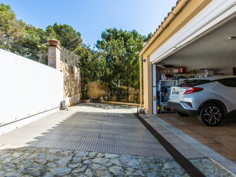 Voiture garée dans un garage spacieux à côté d'une allée en pierre naturelle avec un grand portail coulissant blanc.