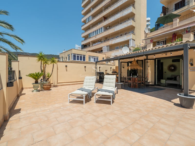 Grande terrasse avec carrelage en terre cuite, deux chaises longues blanches et un coin repas ombragé sous une pergola.
