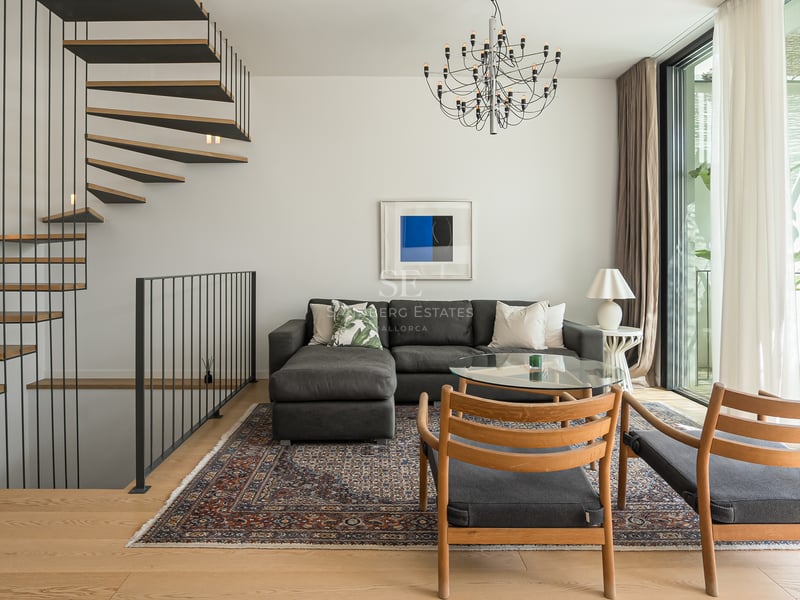 Salon contemporain avec canapé gris, escalier en colimaçon en bois et grandes baies vitrées.