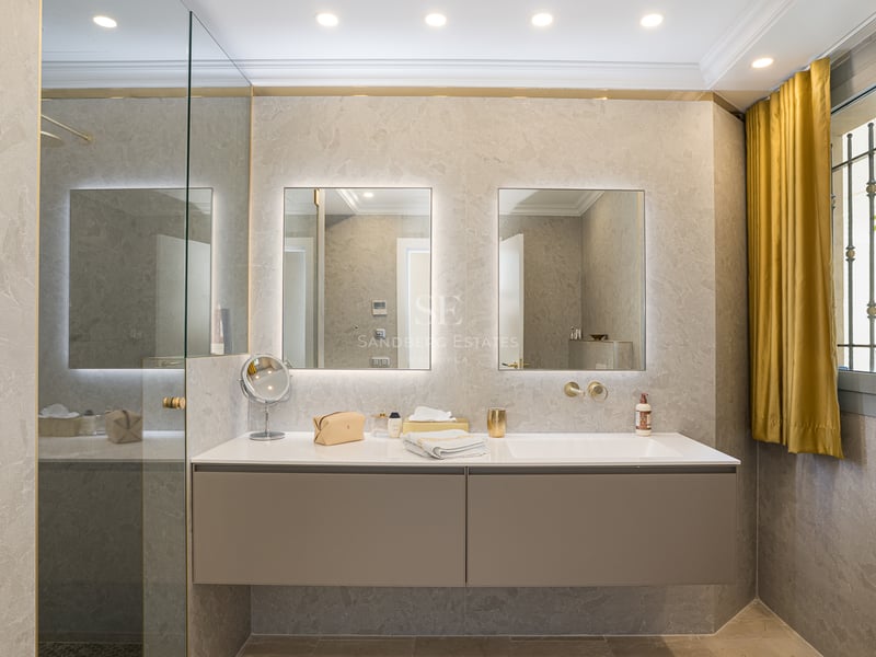 Salle de bains contemporaine avec double vasque suspendue taupe, miroirs rétroéclairés et murs en pierre naturelle.