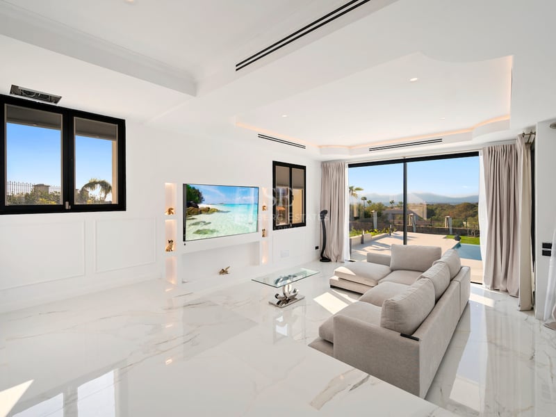 Salon contemporain lumineux avec sol en marbre blanc, grandes baies vitrées coulissantes et télévision murale.